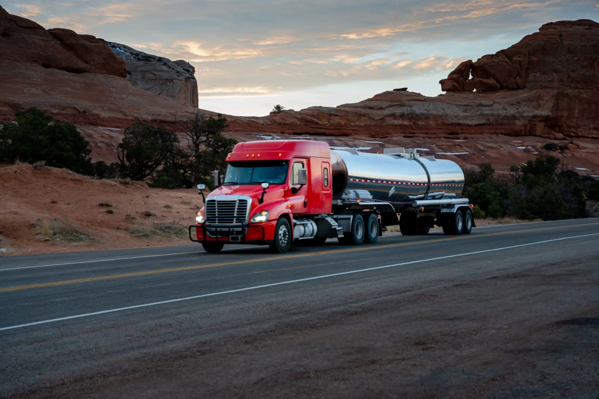 A red semi-truck hauling a silver liquid-bulk tanker trailer.